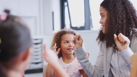 Una-Clase-De-Niños-De-Escuela-Infantil-Usando-Sus-Manos-Para-Contar-Con-Su-Maestra,-De-Cerca