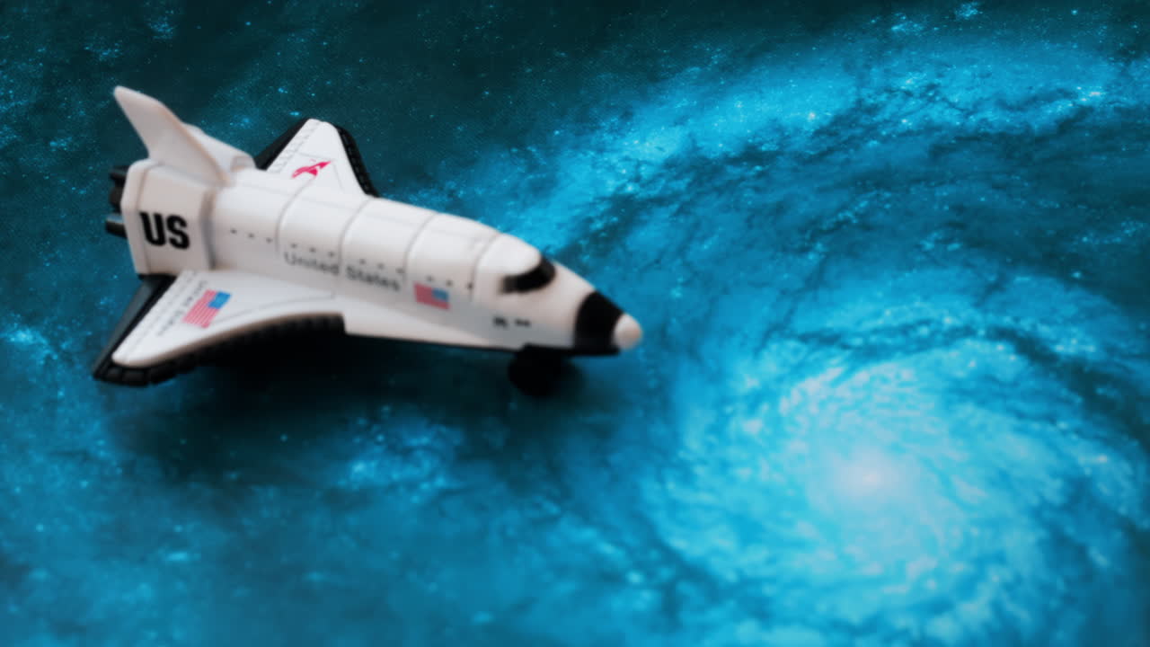 Close up of a miniature toy space shuttle placed on a blue cosmic galaxy backdrop
