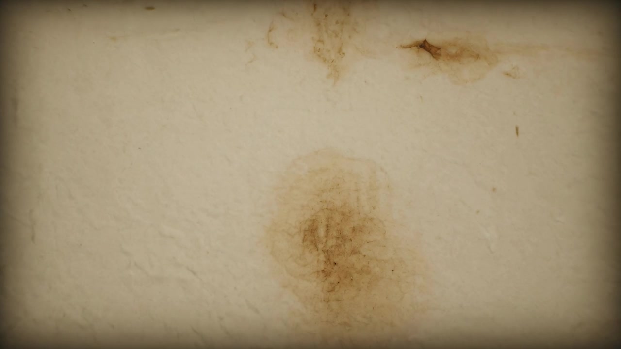 Cámara haciendo zoom revelando una mancha marrón, una imperfección en la parte superior derecha de una pared interior con viñeta, mostrando antigüedad.