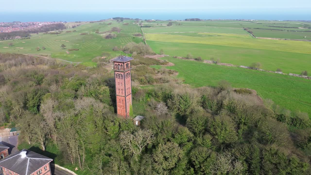 Orbita di un drone attorno alla Torre dell'Acqua di Cleadon a Cleadon, South Tyneside, Inghilterra, spostandosi verso campi rurali con la costa del Mare del Nord visibile all'orizzonte.