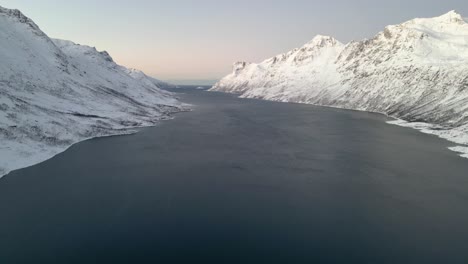 snow-covered mountains flank a serene fjord during twilight, hinting at the peaceful end of a clear day