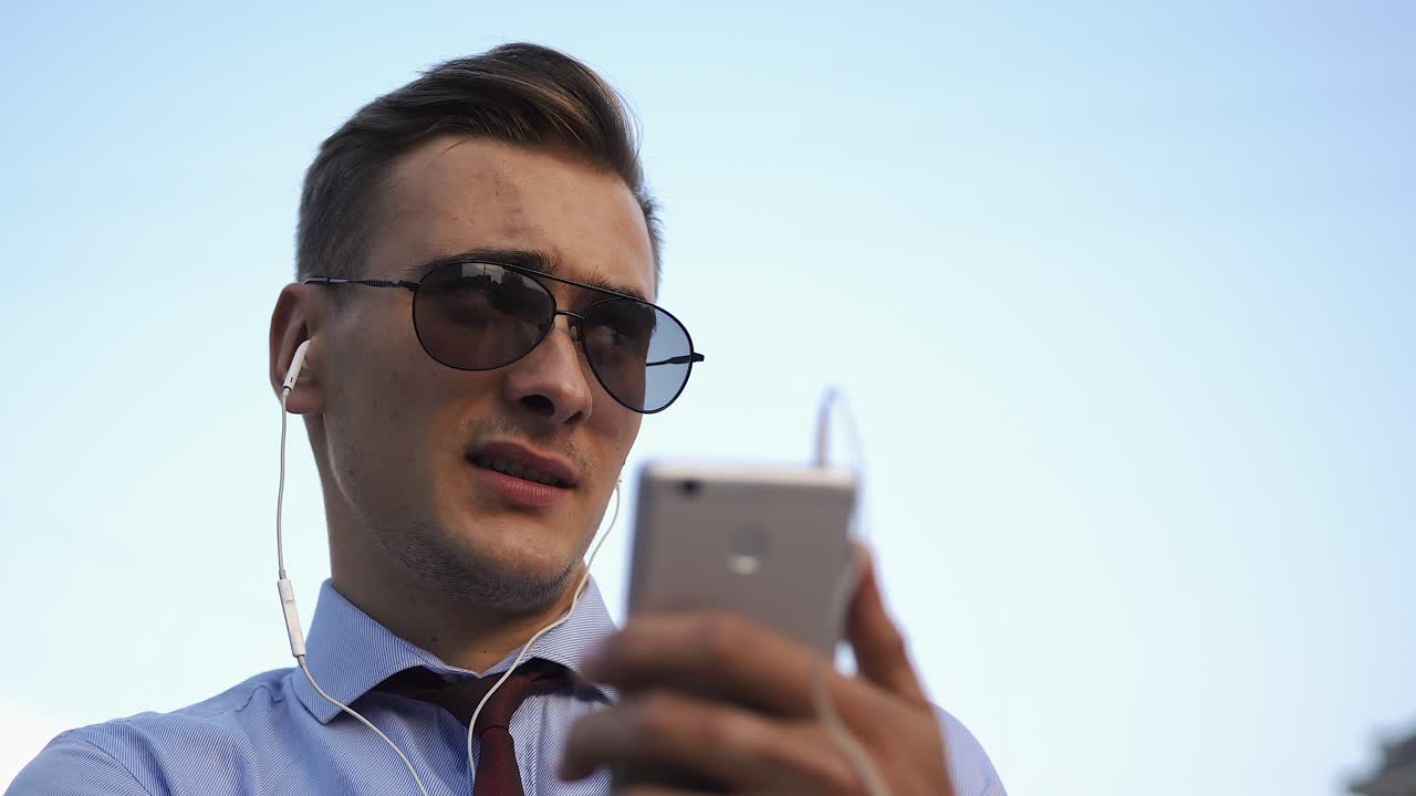 Man with sunglasses and earphones using smartphone outdoors