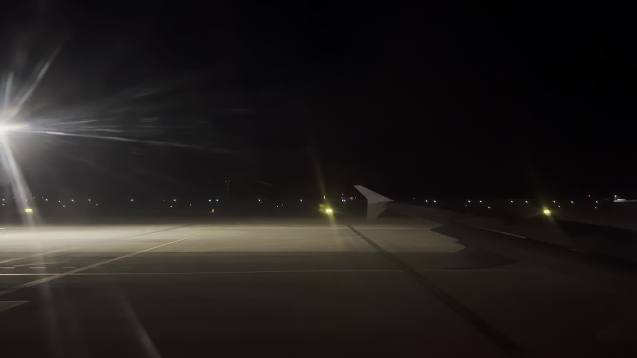 Pemandangan dari jendela pesawat terbang saat pesawat bergerak melalui bandara pada malam hari