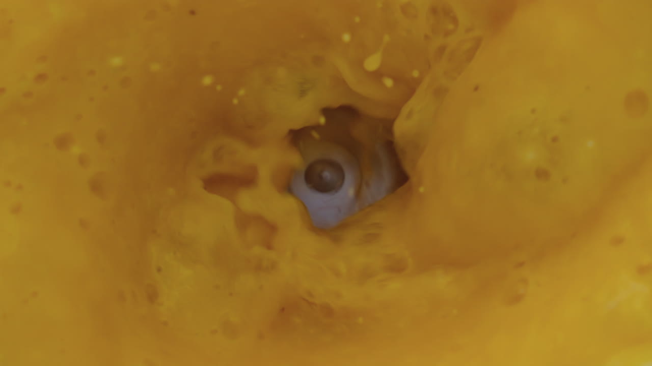 Nærbillede af sprøjtende appelsinsmoothie i blender i super slow motion. Frugter blendes.
