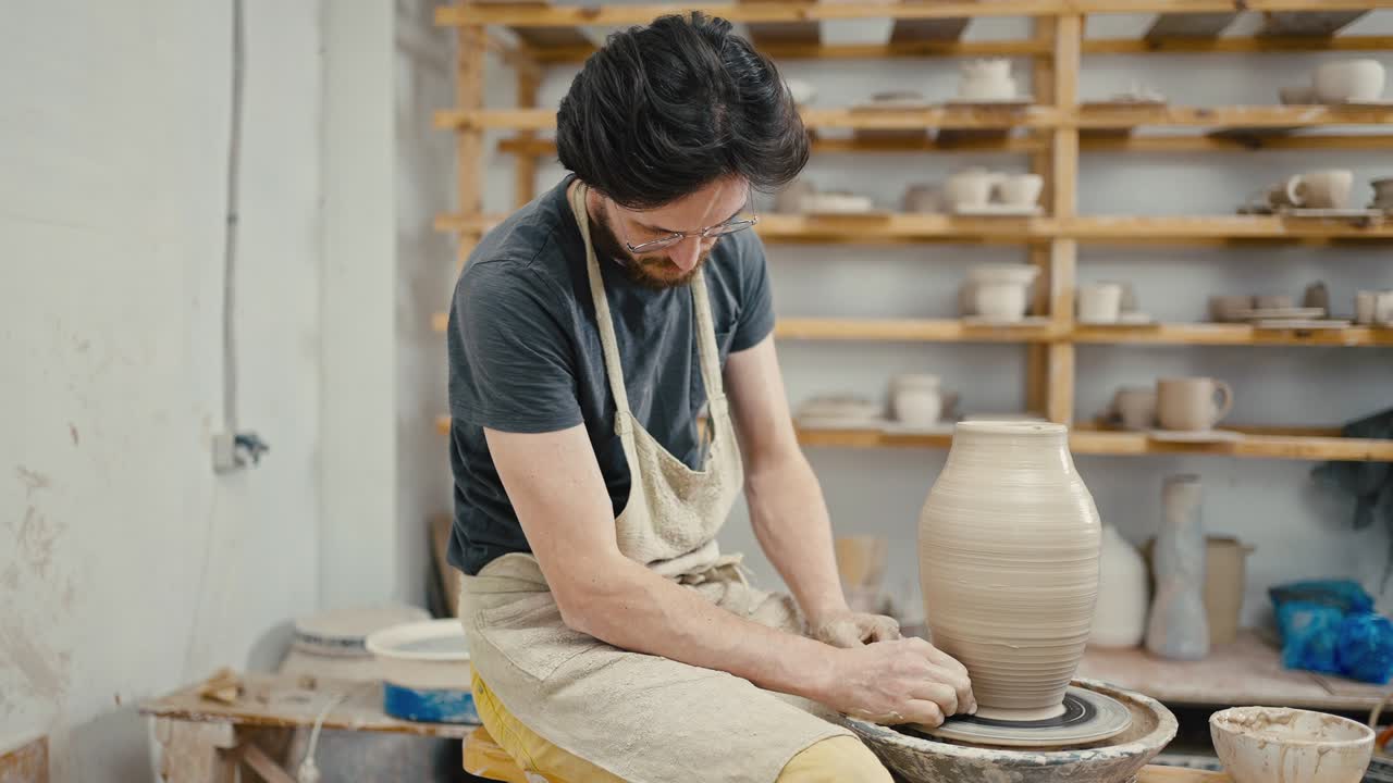 Pottery workshop. Focused man creating handmade ceramic vase on pottery wheel, tracking shot, slow motion
