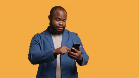 Portrait-of-energetic-happy-man-holding-phone-celebrating,-studio-background