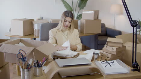 junge kaukasische frau, die ein kleidungsstück im büro einwickelt und verpackt