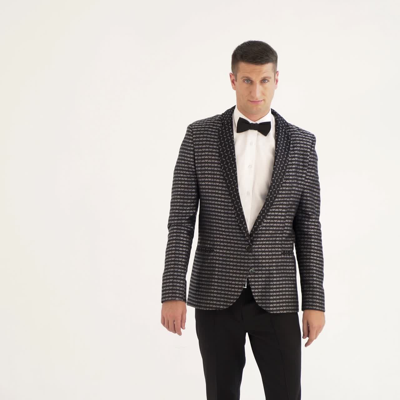 a man in a checkered suit with a bow-tie is parodying manners of macho on a white background in the studio.