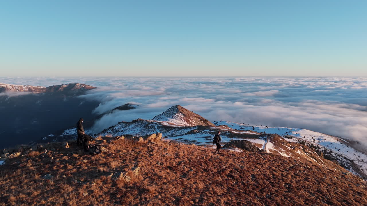 Vista montagna con escursionisti sopra le nuvole nella serena luce del tramonto.