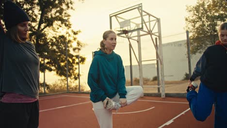 Un-Trío-De-Chicas-En-Ropa-Deportiva-Calentándose-Antes-De-Jugar-Al-Baloncesto-En-El-Patio-De-Recreo-Rojo-Cercado-Por-Una-Valla-Cerca-De-Una-Pelota-De-Baloncesto-Naranja-En-Una-Mañana-De-Verano.