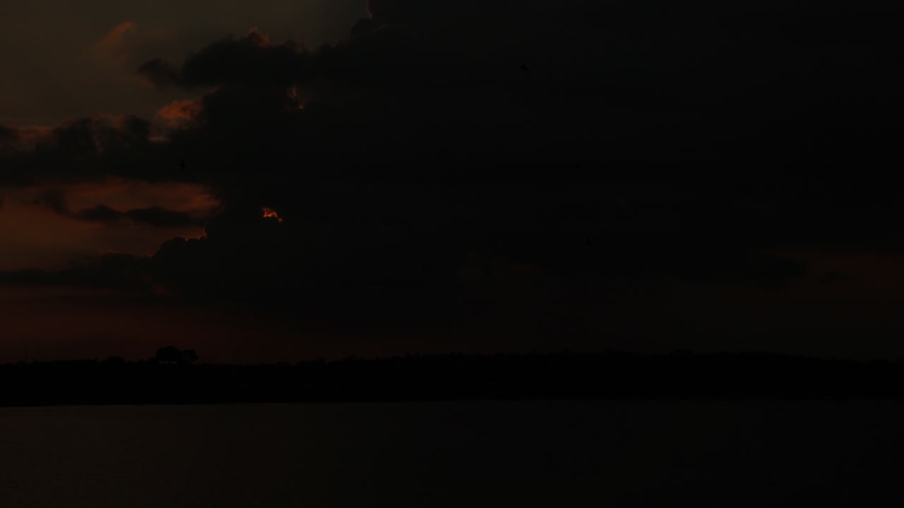 lapso de tiempo de la puesta de sol con rayos de sol reflejados en el agua del río y el sol se pone detrás de las nubes oscuras