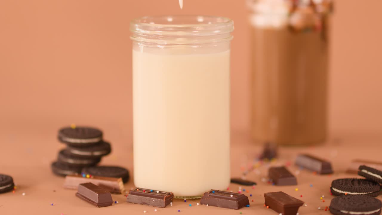 Versamento al rallentatore di un cremoso milkshake alla vaniglia in un barattolo di vetro, con milkshake al cioccolato, biscotti e codette