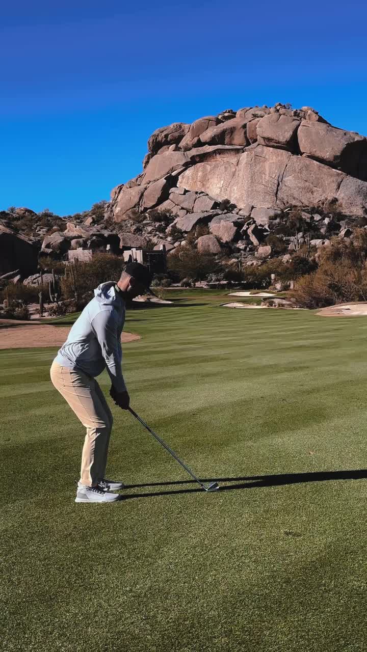 Angry golfer hits bad shot and throws club, pristine desert golf course with rock backdrop, vertical sunny day 4k