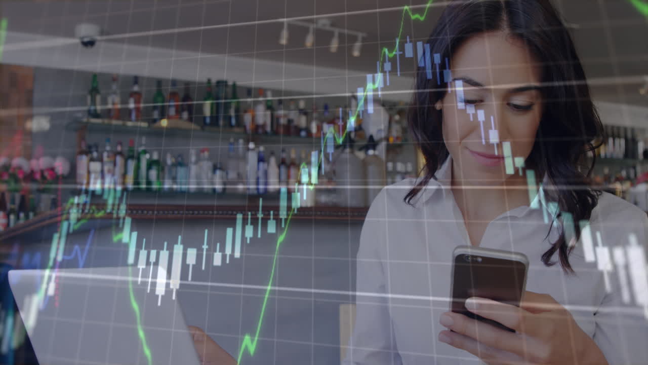 animación de gráficos y números cambiantes, mujer caucásica sonriente con computadora portátil usando teléfono celular