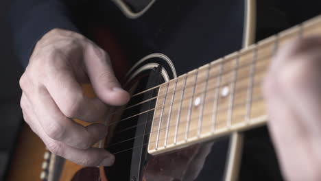 person in pullover plays old black and brown guitar closeup