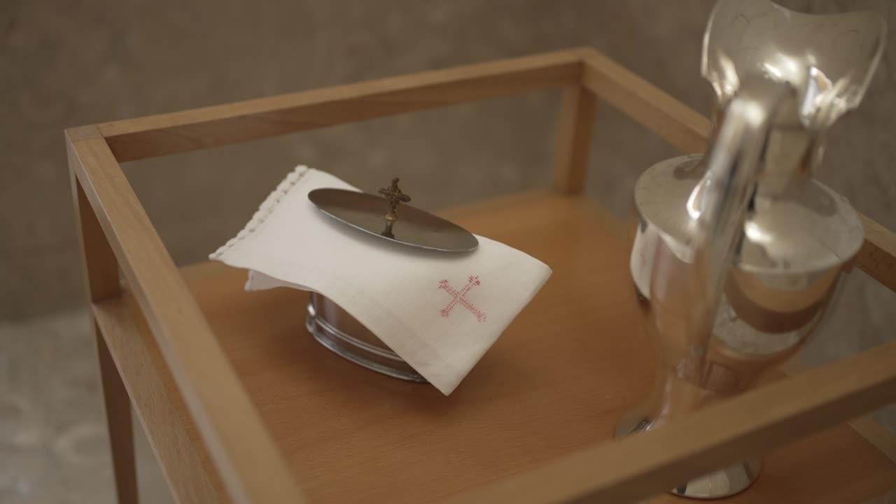 Close up of silver tray with a covered vessel on a wooden table in a baptismal setting.