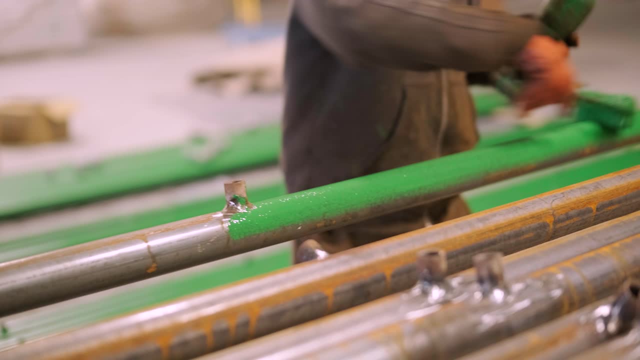 화가 노동자는 큰 건설 현장에서 녹색 롤러로 금속 파이프를 칠하고 있습니다.