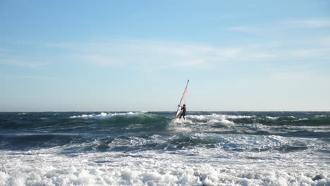 pan shot of a norwegian windsurfer, surfing a wave, at the coast of the north sea, in the atlantic ocean, on a sunny, summer day, in lista, south norway