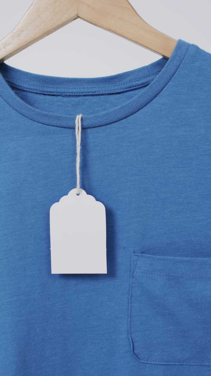 Vertical video of blue t shirt with tag on hanger and copy space on white background