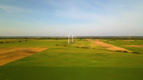 drone shot of two working wind turbines generating green electric energy on a cultivated field on a sunny summer day, use of renewable resources of energy, still shot