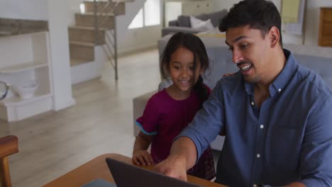 Feliz-Padre-E-Hija-Hispanos-Sentados-En-La-Mesa-Mirando-La-Computadora-Portátil