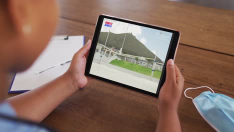 Composite-of-woman-sitting-at-table-with-face-mask,-watching-athletics-high-jump-event-on-tablet