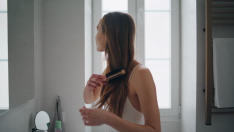 Focused-woman-combing-hair-at-mirror-place-close-up.-Model-making-hairstyle