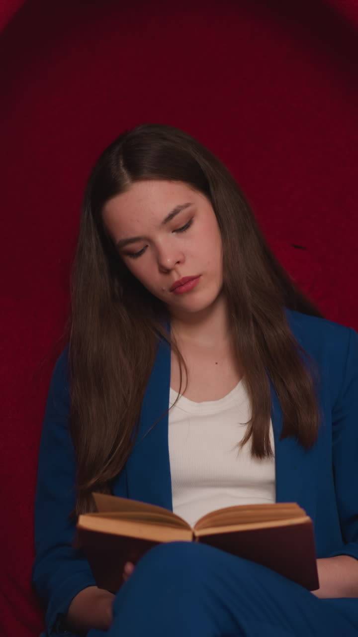 una joven maestra da vuelta las páginas de un libro en la biblioteca. una mujer en uniforme se relaja durante el descanso entre las conferencias en una silla de huevos en la universidad. área de lectura en la universidad