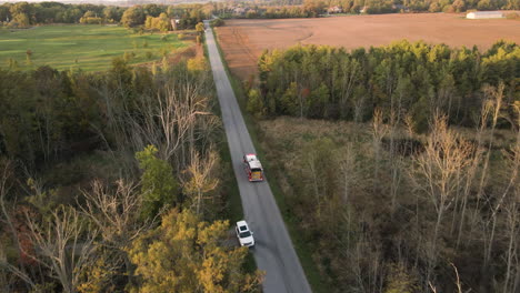 aerial tracking view of emergency fire truck vehicle driving fast along countryside road with flashing lights, rescue first responder mission for fire fighting alert, path route through nature lands