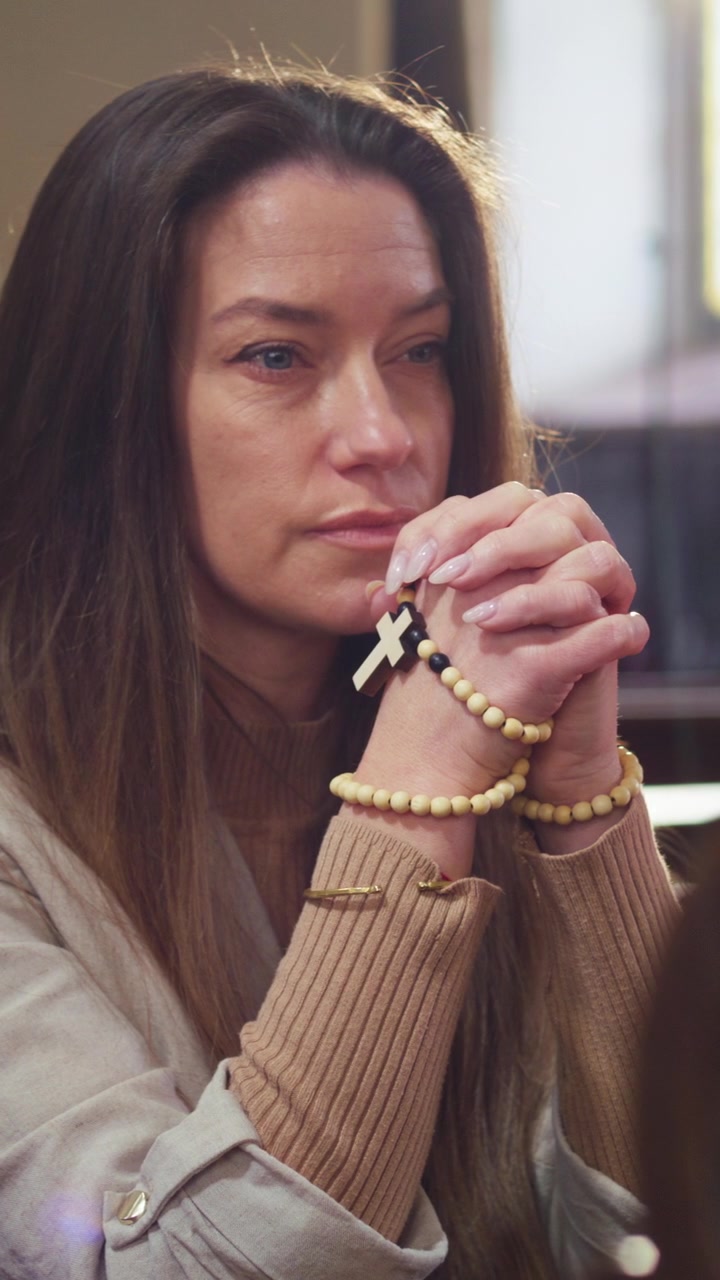Donna seduta in silenziosa devozione, con le mani che tengono un rosario, che prega in un banco di chiesa di legno durante.