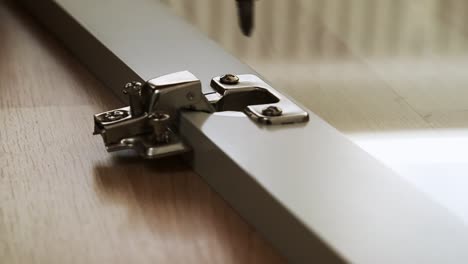 close up of a drill screwing in a screw into a hinge for a glass cabinet