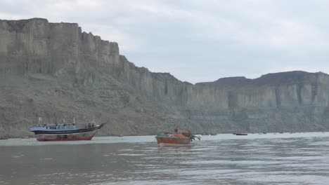 barcos pesqueros amarrados frente a la costa de gwadar en baluchistán con pájaros volando por encima y acantilados vistos en segundo plano