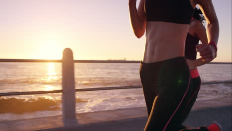 Zwei-Sportliche-Frauen-Laufen-Im-Freien-In-Zeitlupe-Auf-Der-Promenade-Bei-Sonnenuntergang-Am-Meer-Und-Genießen-Den-Abendlauf