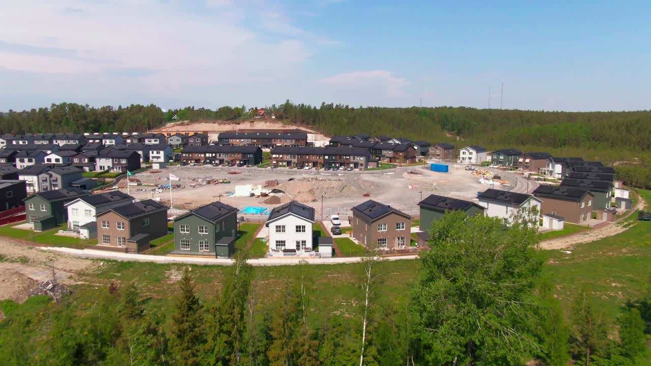 Wide shot illustrating the rapid transition from newly completed townhouses and homes to a raw, dusty construction area and access road