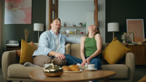 excited spouses laughing sofa interior. happy smiling family having fun at home