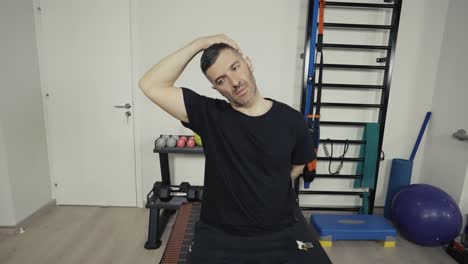 un hombre estira los músculos del cuello antes de hacer ejercicio en su pequeño gimnasio en casa