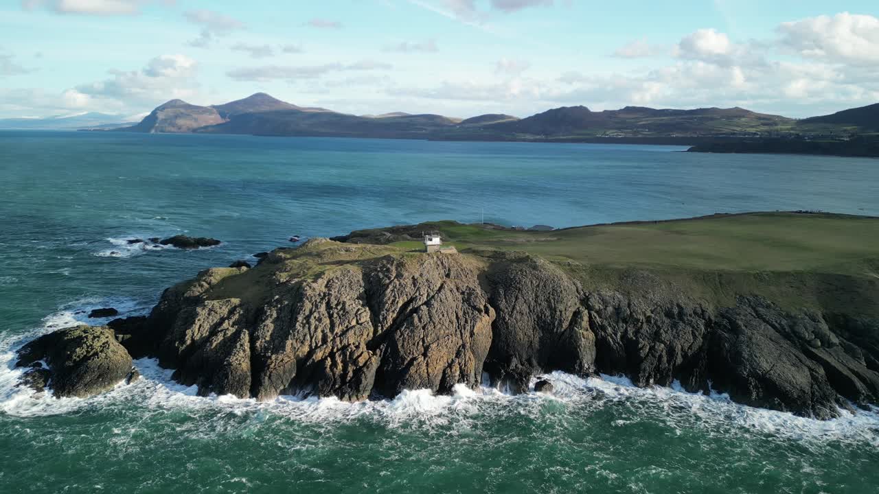 las olas se estrellan en la hermosa costa de gales del norte, un soleado día de invierno. drones aéreos giran alrededor de la estación de observación de coastwatch, nefyn, reino unido.