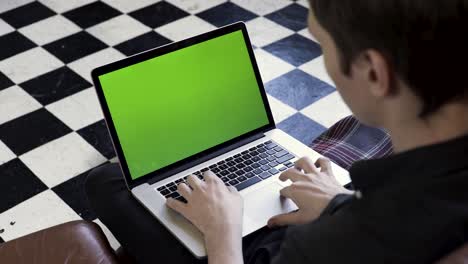 man working on a laptop with a green screen