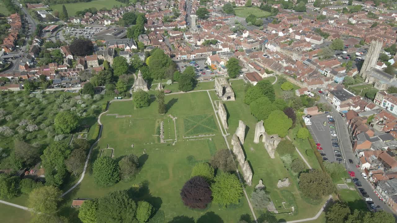 Aerial view of the Glastonbury Abbey ruins an 8th century monastery and gardens. Drone rotating to the left showing the Glastonbury town and the extensions of the abbey grounds. 4K, 60fps.