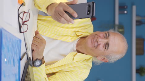 vertical video of home office worker old man talking on the phone facetime happily.