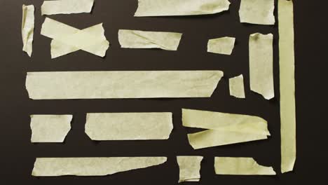 Video-of-close-up-of-multiple-yellow-paper-tape-pieces-on-black-background