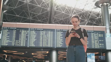 a young woman at the airport with a smartphone near the scoreboard-departures