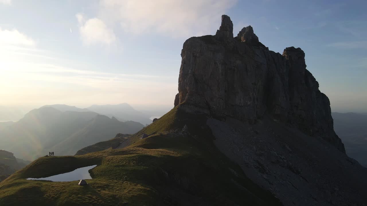 Aerial orbit from dark side of Gross Achslenstock in the Swiss Alps over alpine pond, rugged landscape in Schwyz, Switzerland