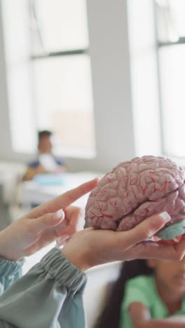 video of happy caucasian female teacher holding brain model in class of diverse pupils