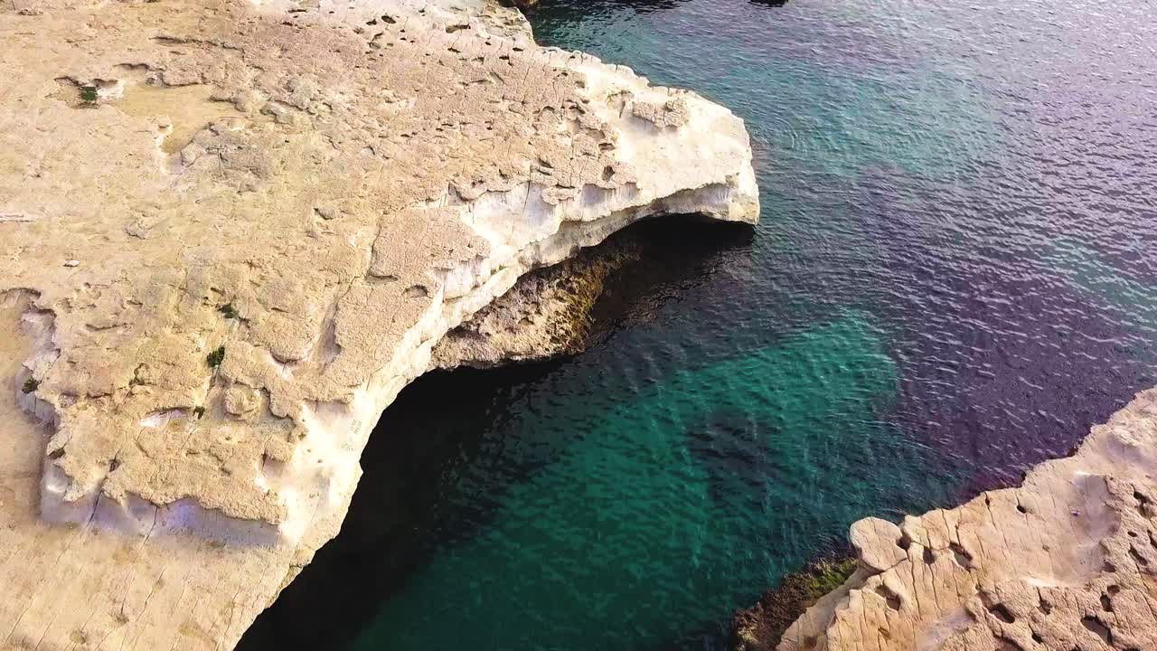 un vuelo temprano por la mañana sobre la pintoresca piscina de san pedro, malta, que muestra las rocas de arenisca dorada y las cristalinas aguas azules del mar medaterainan.