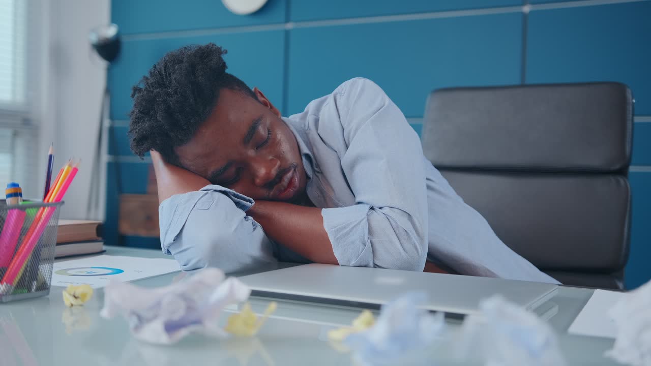 Young african american man sleeping putting head at workplace near laptop