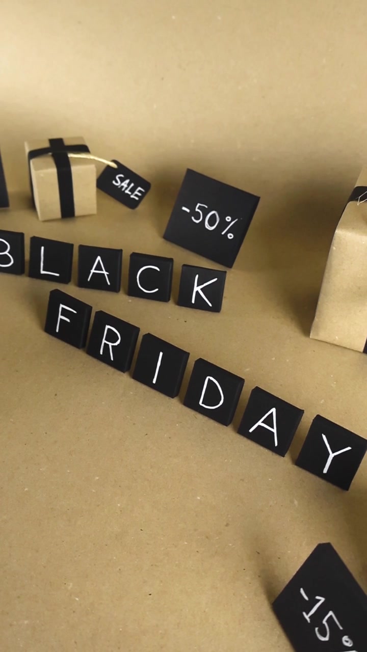 Siyah fayanslar üzerindeki Black Friday yazısının üzerinde kayan kamera, açık kahverengi bir arka plan üzerinde kraft kağıdı hediye kutuları ve çeşitli indirim yüzdesi işaretleri ile perakende promosyonları için mükemmel