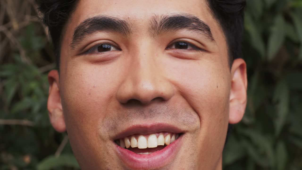 Adult Asian male starting with smile then shifting into laughter in garden under overcast daylight