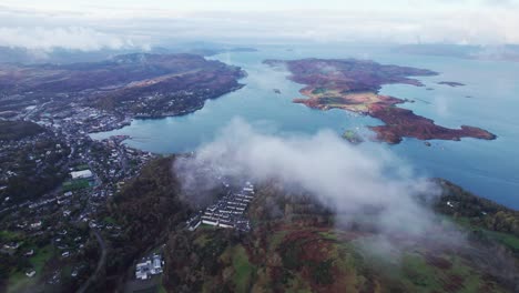tiro aéreo descendente a través de nubes brumosas que revelan el impresionante pueblo pesquero de oban, escocia, mull island y drones de las tierras altas del oeste