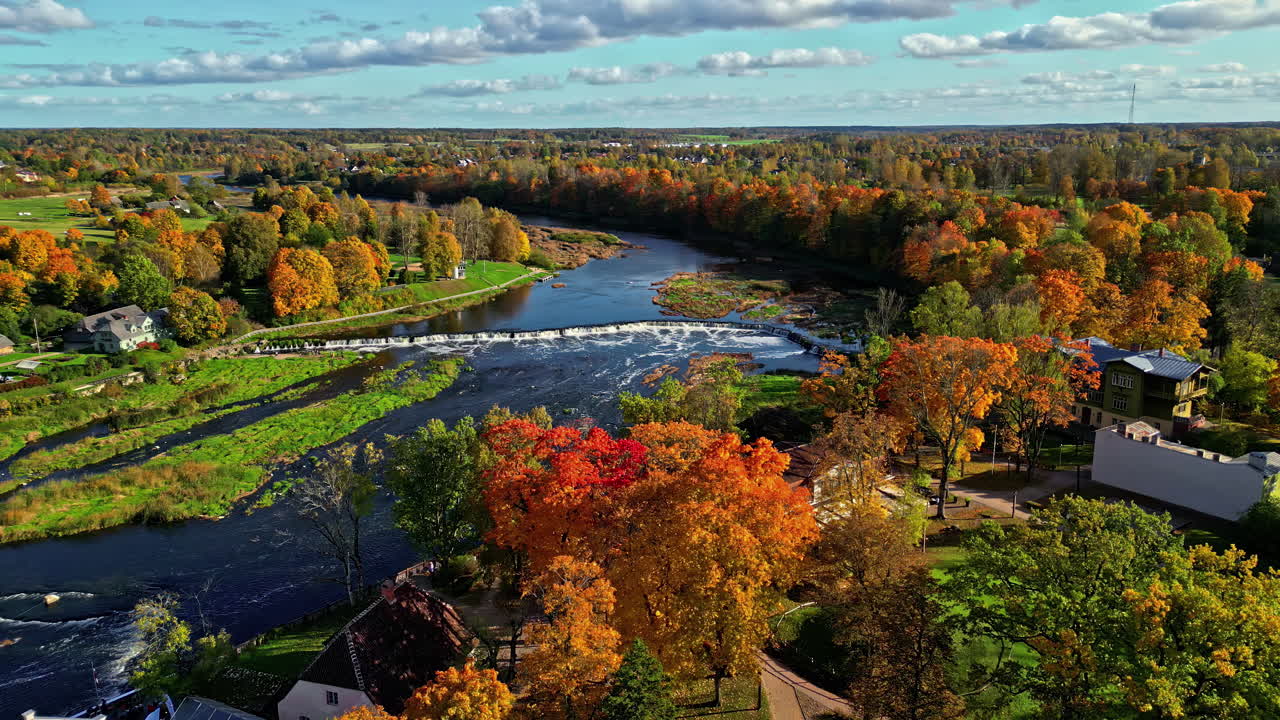 Aerial over autumn maple trees toward Venta Waterfall on partly cloudy day